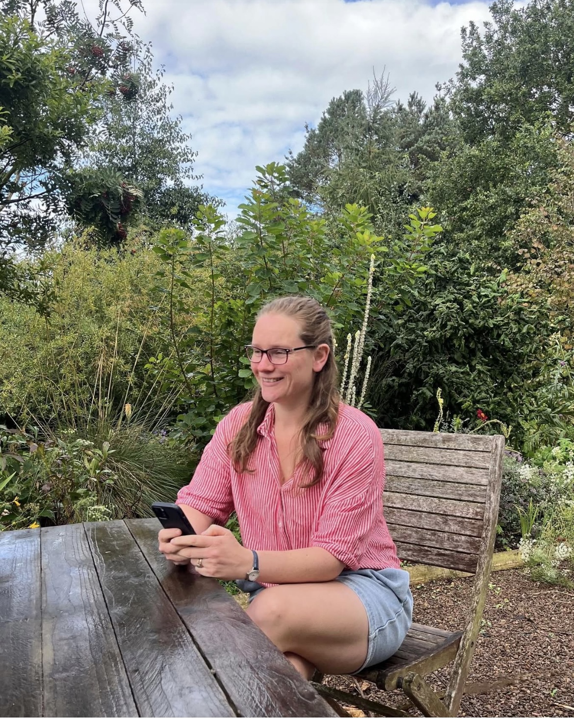 Client sitting outdoors at a wooden table in natural light, relaxed and focused on her phone