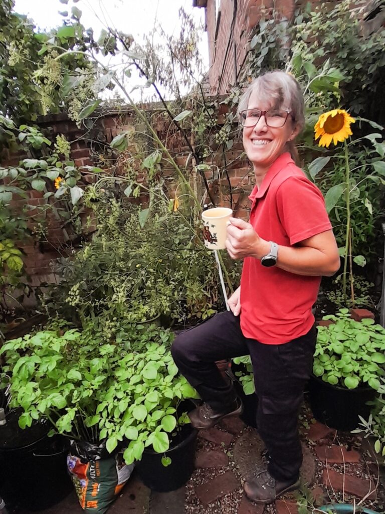 Woman holding a mug in a garden surrounded by plants