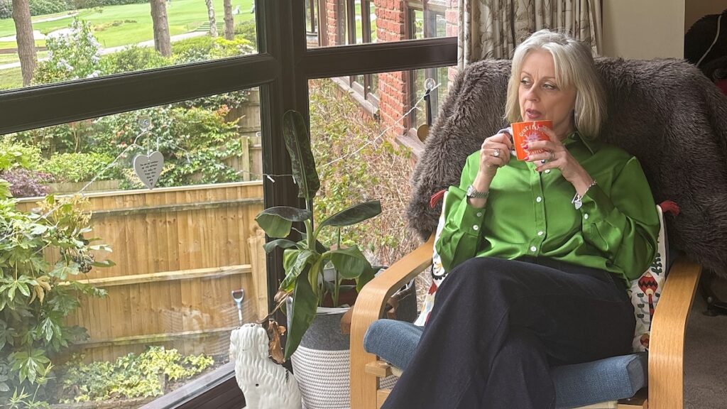 Business owner relaxing with a cup of tea beside a window during a guided virtual brand photo shoot in her home.
