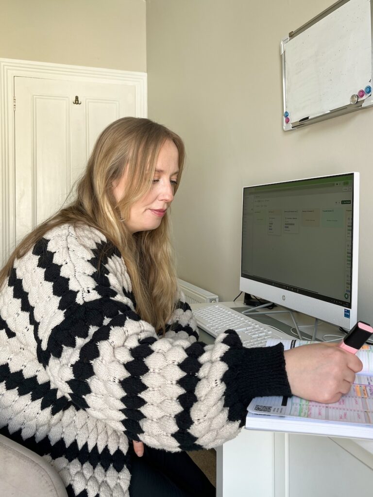 Betsan sitting at her desk, holding a highlighter while marking notes in a notebook, with her computer open beside her.