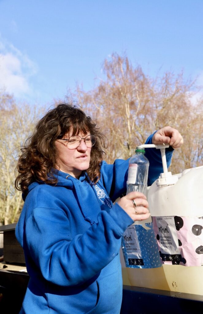 Natasha filling a reusable bottle with eco-friendly cleaning liquid from a refill container on her narrow boat.
